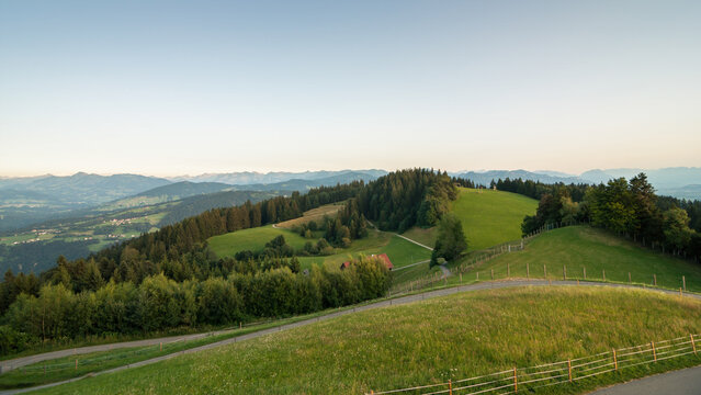 View from the top of Pf&auml;nder mountain at sunset - view at green alpine meadows, Bregenz Forest and range of Vorarlberg alpine summits in the background. Clear sky without gradient, calm evening.