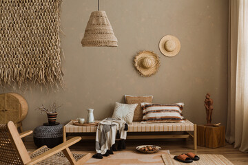 Interior design of ethno style living room with rattan furniture, daybed, pouf, hanging decoration on the wall, lamp and elegant personal accessories. Home decor. Template.	