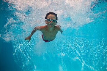 Kid boy with goggles swimming underwater joyfully after dive - 755577943