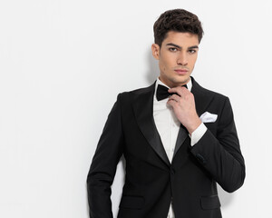 sexy young businessman in black tuxedo adjusting black bowtie
