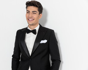 happy elegant groom in black tuxedo looking away and laughing