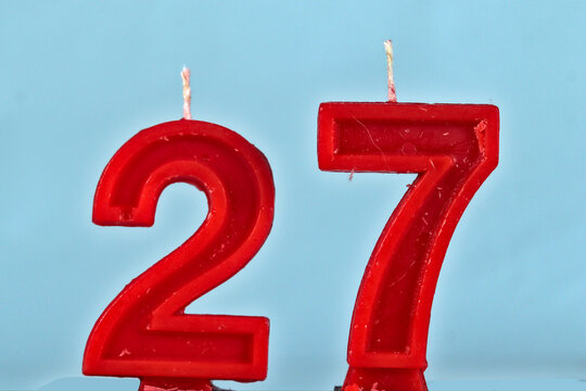 close up on red number twenty seventh birthday candle on a white background.
