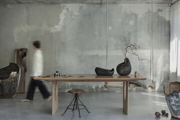 Raw composition of japandi dinning room interior with walking woman, wooden table, gray concrete...