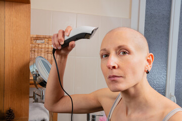 Hairless lady look at camera uses electric razor to shave head - 755581383