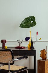 Modern composition of workplace interior with black desk, rattan chair, colorful sculpture, vase...