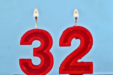 close up on a red number thirty two birthday candle with fire on a white background.

