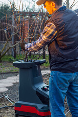 Male gardener using electric garden grinder to shred cut tree branches during spring cleaning. Cleanup around the house. Spring gardening. Pruning trees.