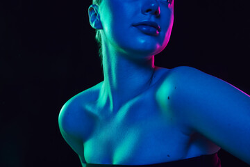 Cropped photo of young female neckline with smooth, healthy skin in neon light against black studio...