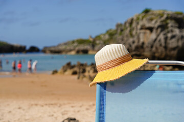Fototapeta na wymiar A beach scene with a yellow hat on top of a beach chair. Summer holidays on the coast
