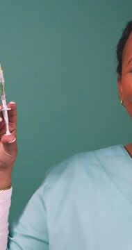 Friendly young Black doctor holds up injection needle syringe, squirts medicine