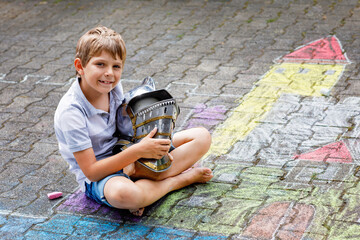 Little active kid boy drawing knight castle and fortress with colorful chalks on asphalt. Happy...
