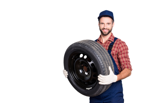 Portrait with copy space, empty place for advertisement of joyful cheerful mechanic in blue overall, shirt having, holding tire in arms, looking at camera, isolated on grey background