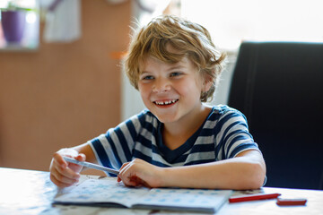 Portrait of happy boy doing homework in kitchen at home. Elementary school studing writing and learning. Smiling child.