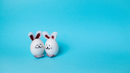 Two cute Easter bunnies made of white chicken eggs. Happy Easter Bunny Day Concept. Light blue...