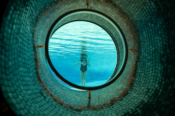 Woman Standing in the Ship Porthole in Underwater in Swimming Pool in a Sunny Day in Switzerland.