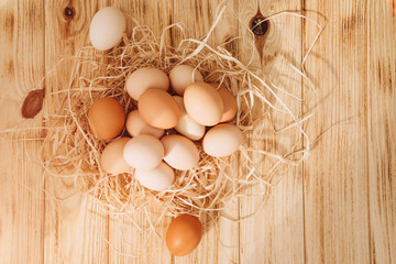 Chicken eggs of different brown and beige shades on a wooden background with dry corn. Easter...