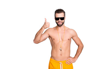 Portrait of fit sportive lifeguard with stubble in yellow shorts holding hand on waist showing thumb up sign isolated on grey background