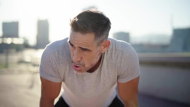 Middle-aged Caucasian man exhausted after running outdoors, taking a break to breathe and recover energy to continue exercising. Healthy and sporty people. Copy space.