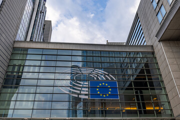BRUSSELS, BELGIUM, June 23, 2023: A view of a contemporary building displaying the European Union flag, set against a backdrop of a partly cloudy sky. European Union Flag on Modern Building Facade - obrazy, fototapety, plakaty