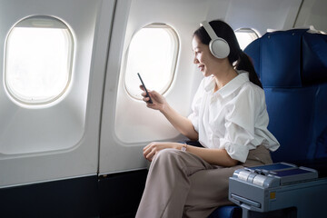 Asian young woman wearing headphone listen to music at first class on airplane during flight,...