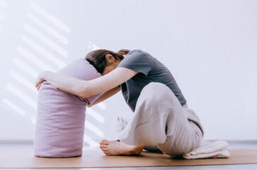 Woman in casual clothing practicing yin yoga butterfly pose leaning on bolster