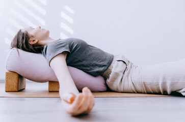Woman in casual clothing doing yin/restorative yoga with bolster supported by blocks