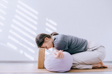 Woman in casual clothing doing yin yoga crossed arm stretch with bolster and cork block
