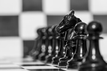 Detalle de  la figura del caballo entre los peones de un tablero de ajedrez, en blanco y negro - obrazy, fototapety, plakaty