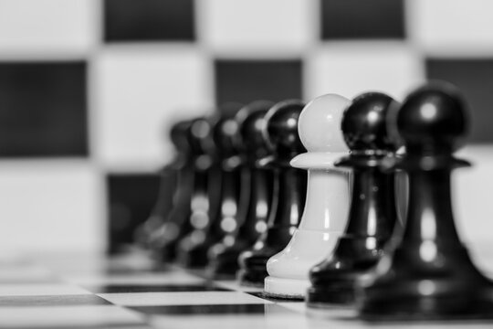 Detalle de un pe&oacute;n blanco entre los peones de color negro en un tablero de ajedrez	