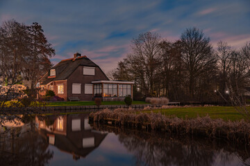 Fototapeta na wymiar Night landscape with starry sky in the Dutch village of Streefkerk. Houses with bright light reflecting in the shine of the water in the autumn season