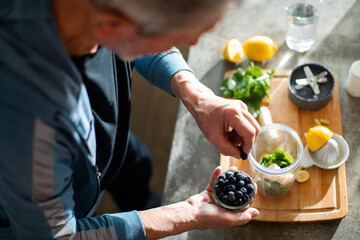 Senior man preparing healthy smoothie with blueberries and greens at home