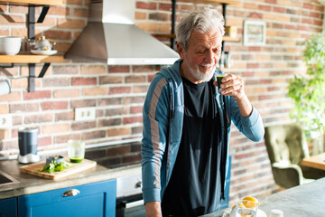 Senior man drinking healthy smoothie in the kitchen at home