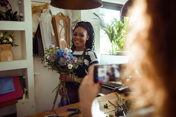 Happy African American female florist being photographed in her flower shop