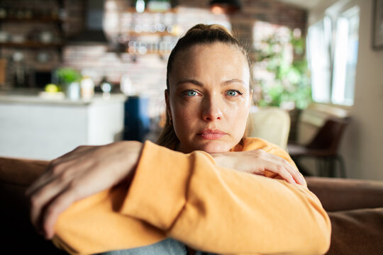 Pensive woman sitting on couch at home with a contemplative expression