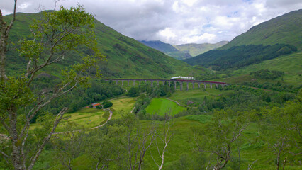 AERIAL: Jacobite steam train crossing Glenfinnan Viaduct in Scottish Highlands