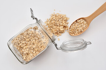 Oat flakes in glass jar with spoon full of oatmeal on white background. Top view. Healthy food for breakfast - 755642915