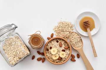 Oatmeal in a wooden bowl with almonds and pieces of banana ready to cook, honey, scattered oat flakes and spoon. View from above. Place for text - 755642939