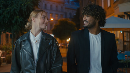 Couple Indian Latino Arabian man and European woman walking city center night outside together pastime tourism tour sightseeing atmosphere date relationship friendship communicate stroll talk weekend