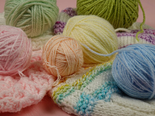 Knitted items from multi colored yarn and a set of the different balls of wool for hand knitting on a pink background