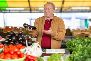 Smiling mature male seller passing eggplants through counter to buyer at local market