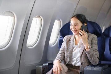 Young asian woman sitting on seat in airplane and talking by smartphone. Young woman traveller talking on cell phone