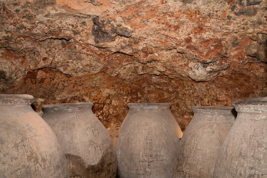 Row of large, old clay jars for wine storage line the stone walls of an underground winery cellar in Chinchon, reflecting centuries-old winemaking traditions