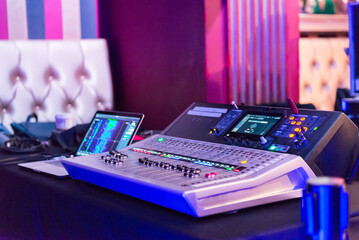 Professional audio mixing console equipped with multiple sliders and screens, ready for managing sound at a concert venue with vibrant lighting