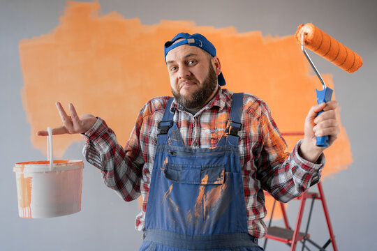 Portrait of a bearded surprised painter holding a bucket and a paint roller.