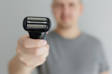Close up of electric razor in male hands in grey tshirt
