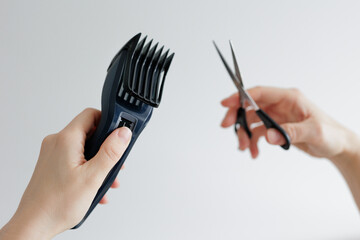Female hands holding hair clipper and scissors on white