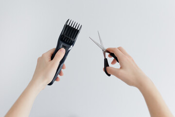 Close up of female hands holding electric hair clipper and scissors on white - obrazy, fototapety, plakaty