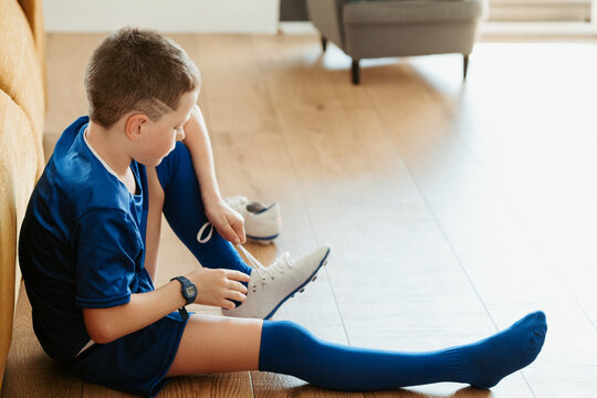 Young boy in soccer gear tying shoelaces indoors - Powered by Adobe