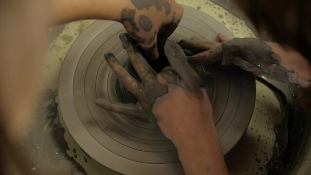 Close-up of potters' hands making a clay vase on a potter's wheel in a workshop. A pottery workshop.