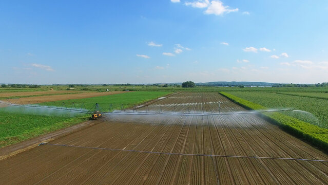 Pouring of farm field with long tubes on tractor at summer sunny day. Aerial view